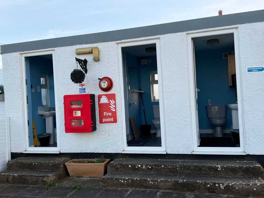 Public restroom exterior with three blue stalls, red fire equipment, and white walls