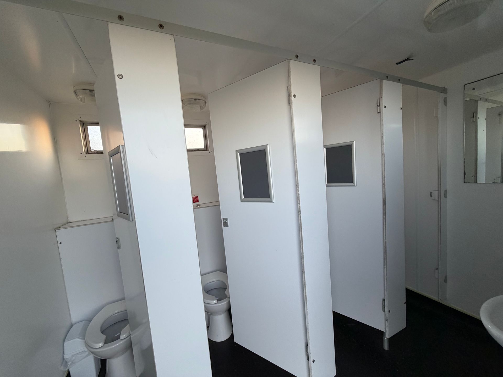 White restroom with multiple toilet stalls and sinks, viewed from the doorway.