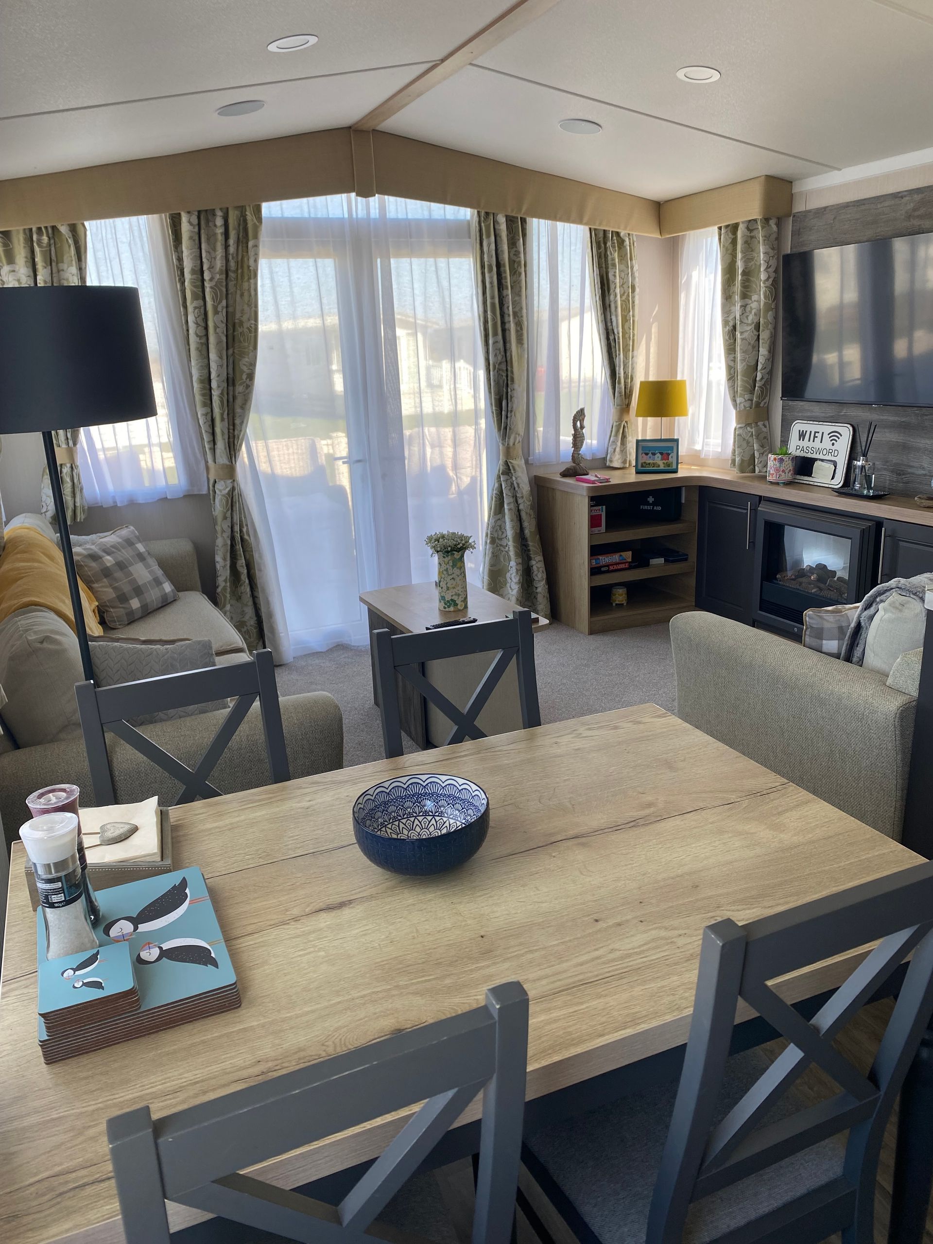 Bright, airy living room with dining table, sofa, chairs, floor lamp, and large windows with curtains