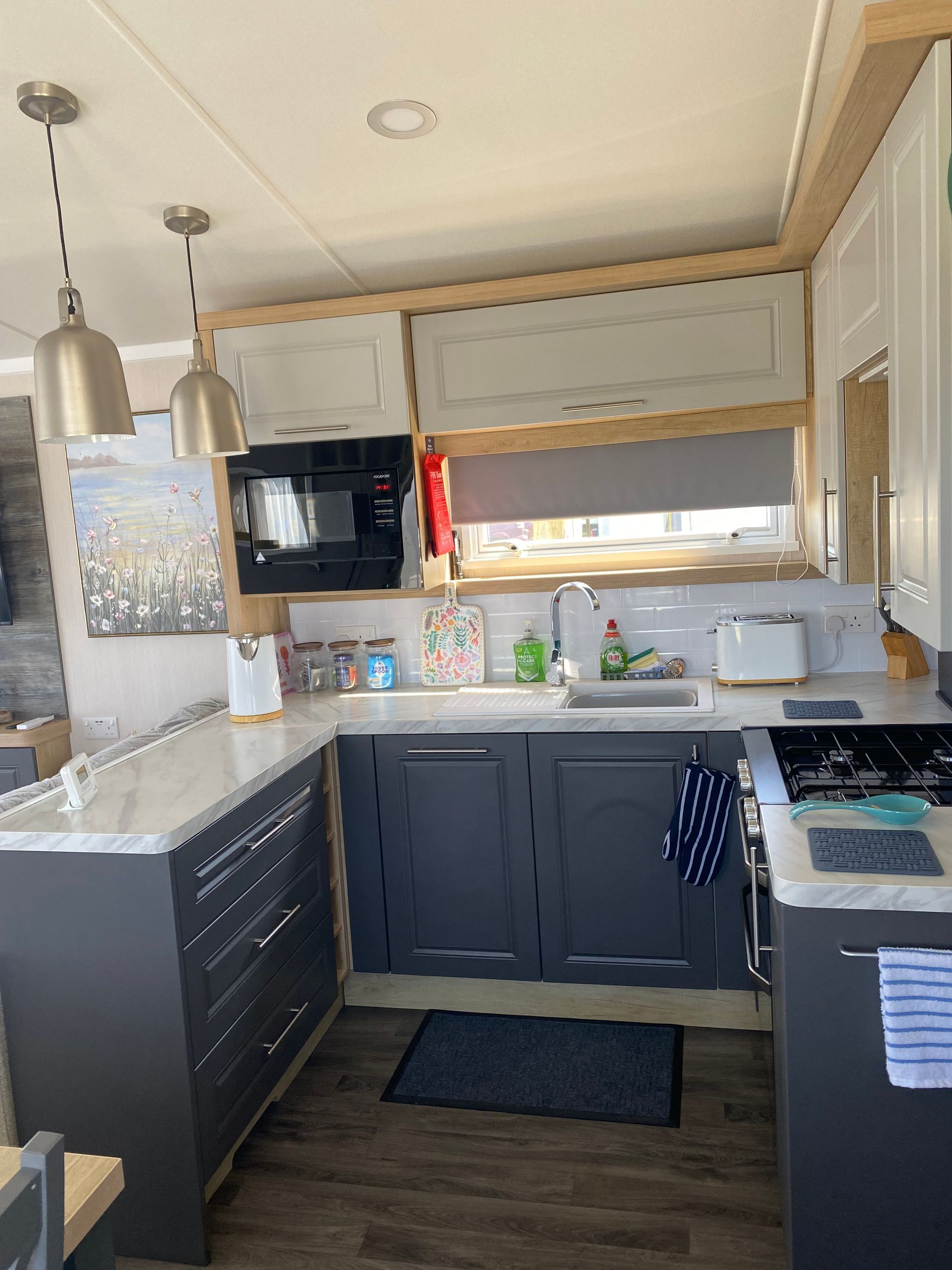 Compact kitchen with gray cabinets, white counters, pendant lights, and a sunlit window above the sink.