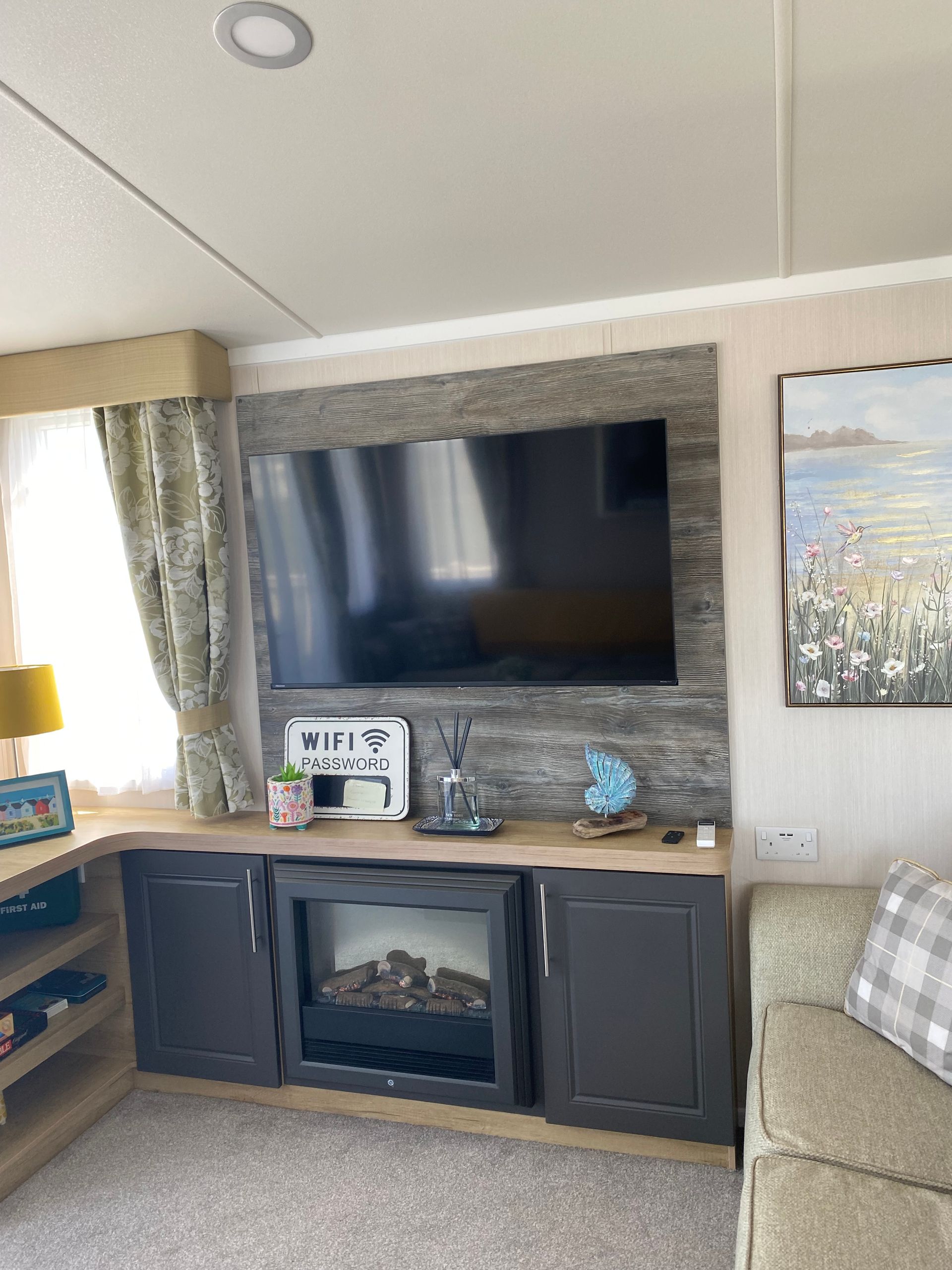 Living room wall with mounted TV, electric fireplace, and dark cabinets beneath a wood mantel