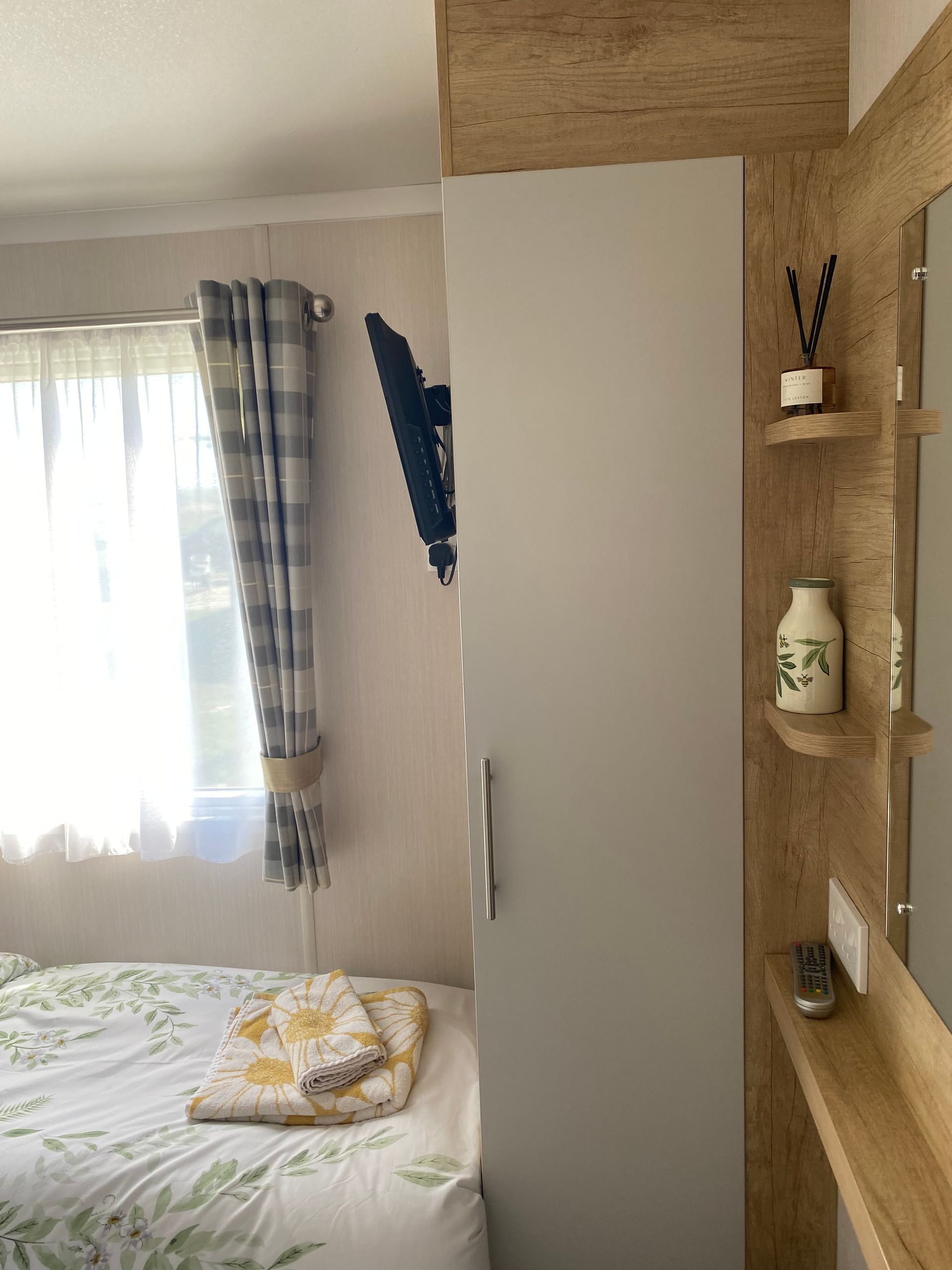 Small bedroom with a bed by a window, white wardrobe, and wooden shelves on the right.