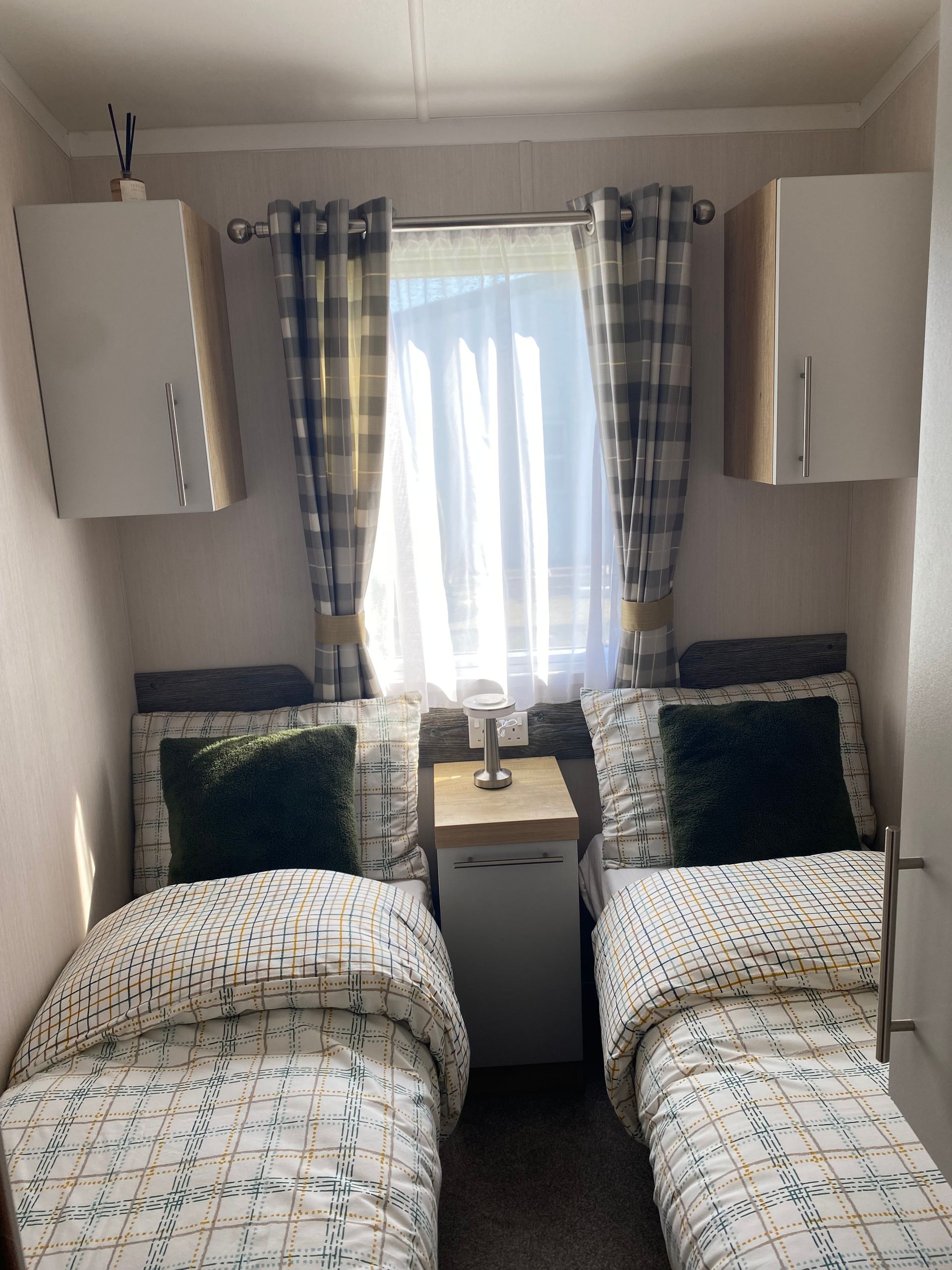 Cozy twin bedroom with patterned bedding, navy pillows, and a bright window between matching cabinets