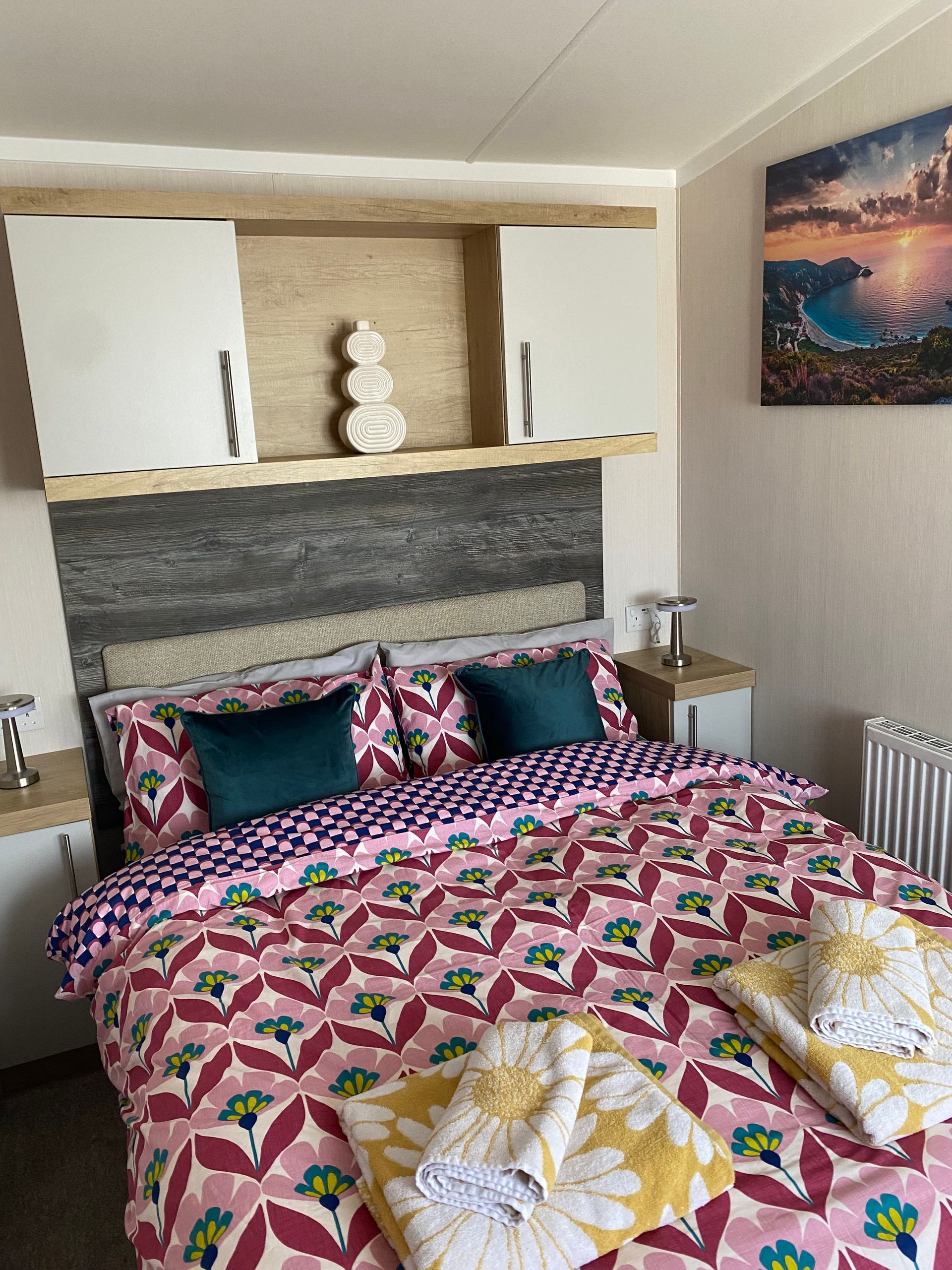 Cozy bedroom with patterned bedspread, decorative pillows, and wall shelf above the headboard