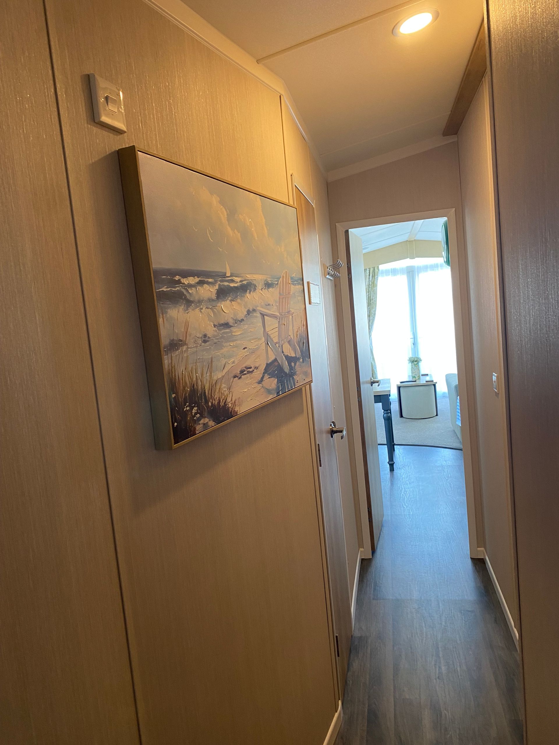 Narrow hallway with framed wall art leading to a bright living area and window