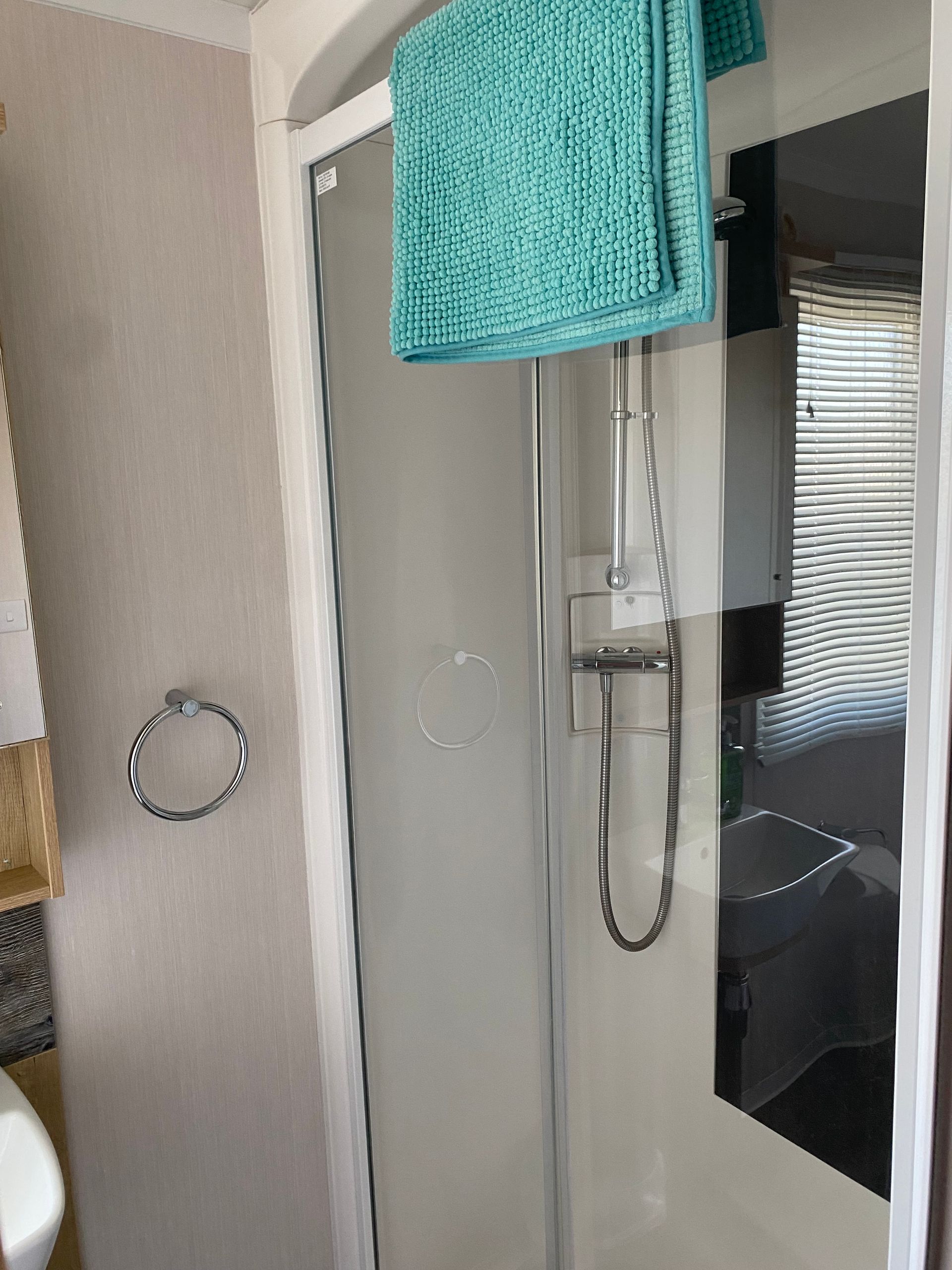 Shower stall with glass door, chrome showerhead, and turquoise towel hanging above it.