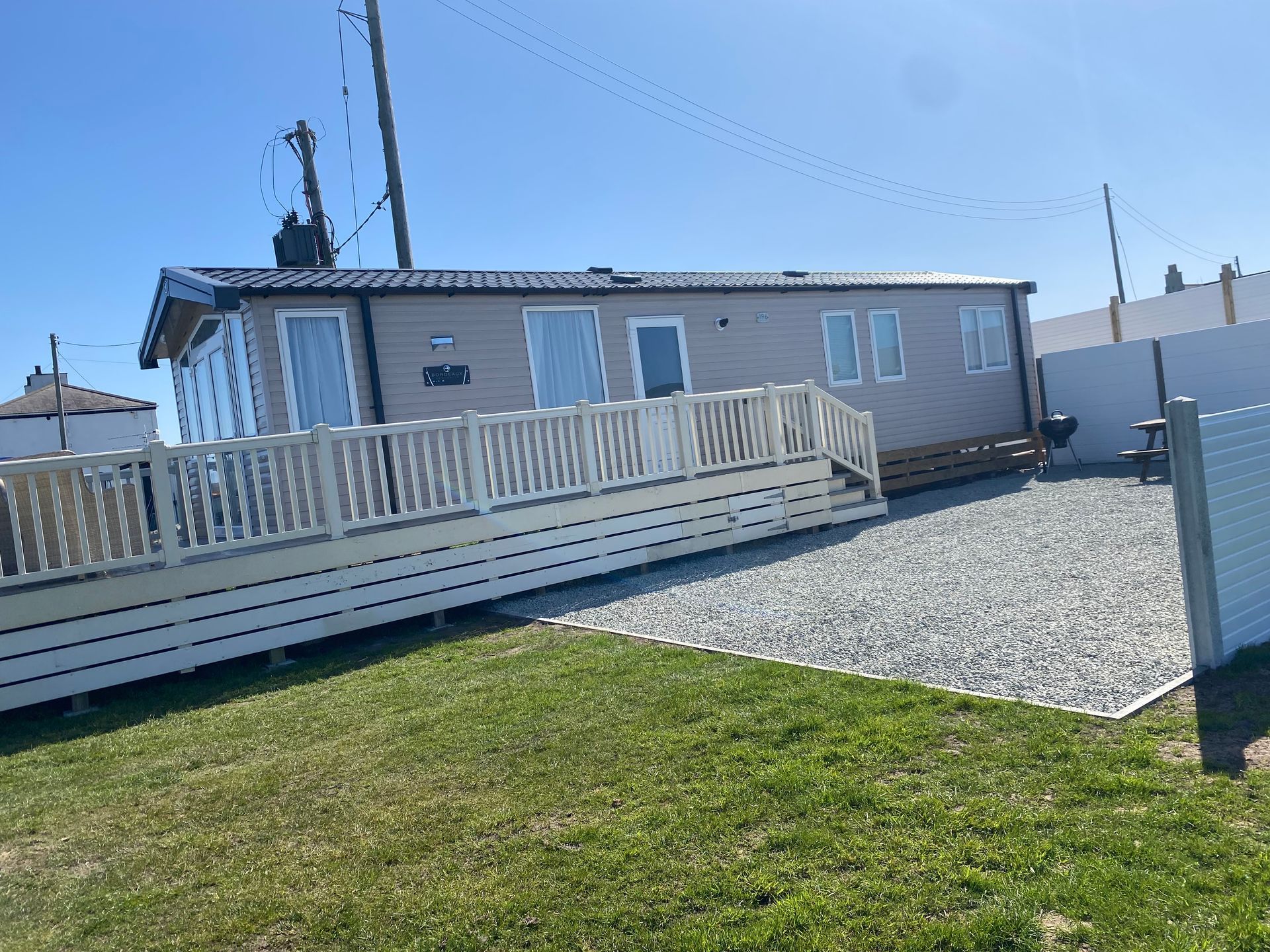 Accessible ramp leading to a beige mobile home beside a gravel lot under a blue sky