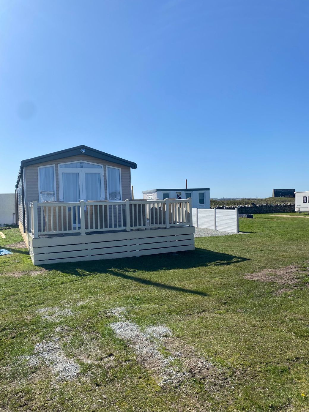 Small white cabin with a deck in a sunny grassy field under a clear blue sky