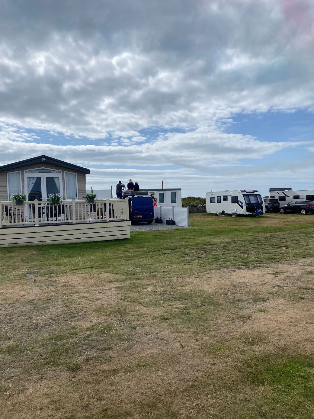 Cloudy beachside campsite with small cabins and parked RVs on a grassy field