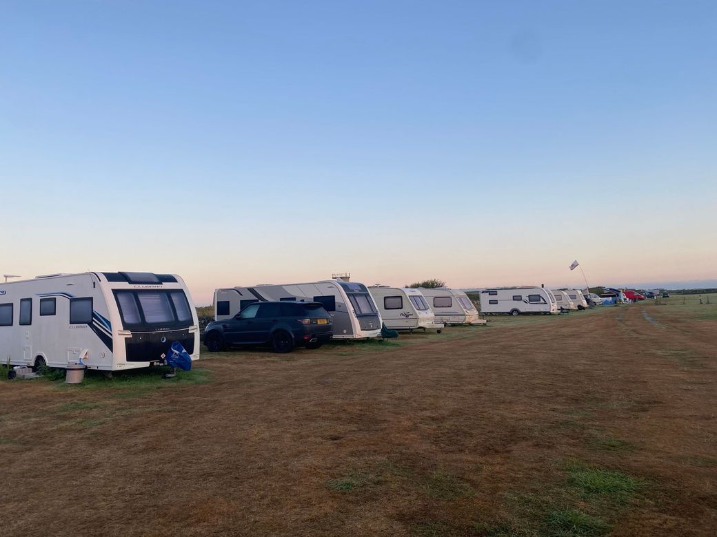 Caravans lined up in a grassy field under a clear blue sky at sunset