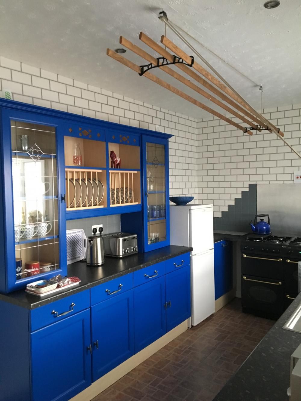 Blue cabinets and white tile kitchen wall with hanging laundry rack and stove on the right