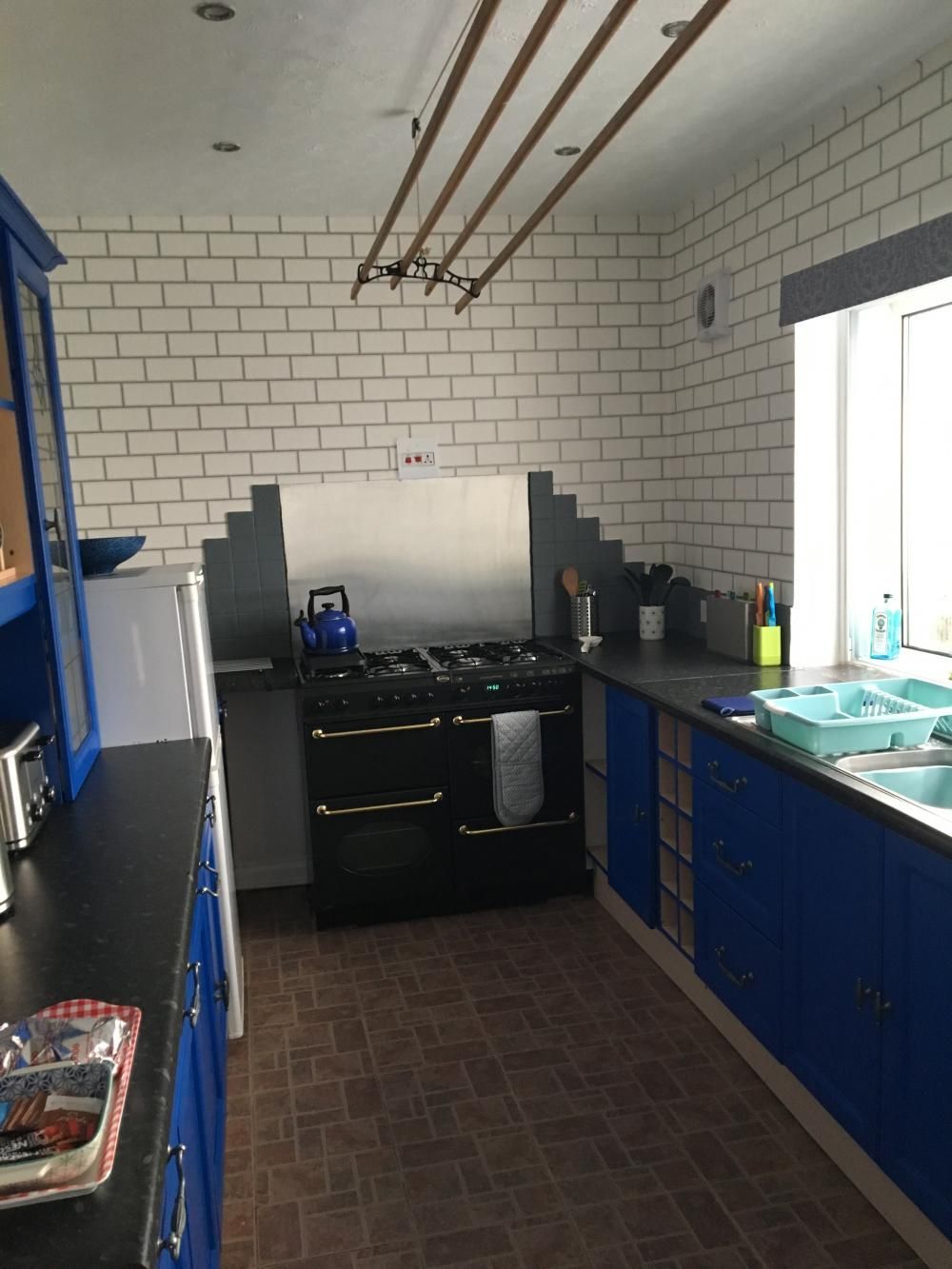 Small kitchen with blue cabinets, white tiled walls, black stove, and a window over the sink.