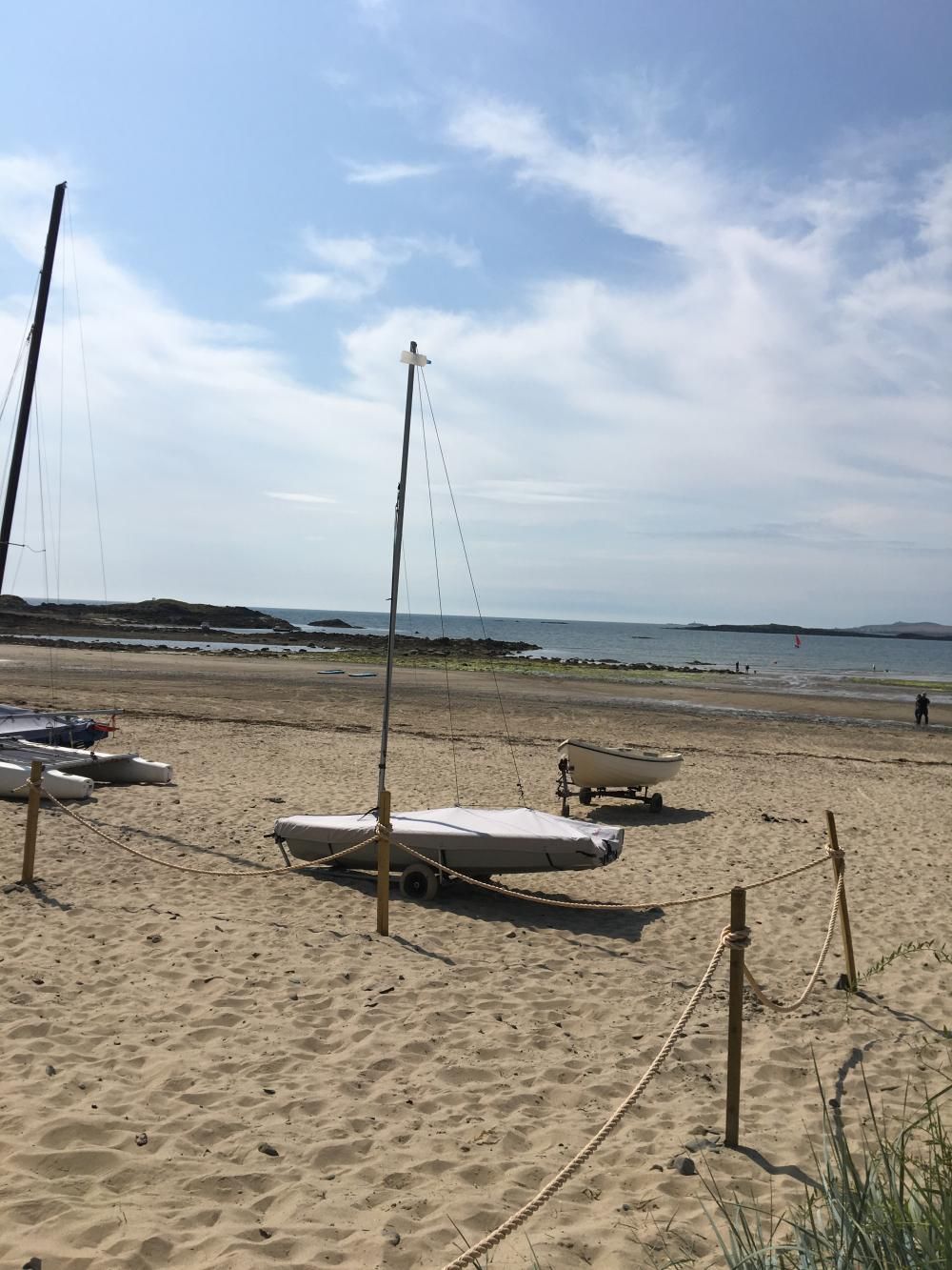 Sandy beach with several sailboats on the shore under a blue sky with clouds