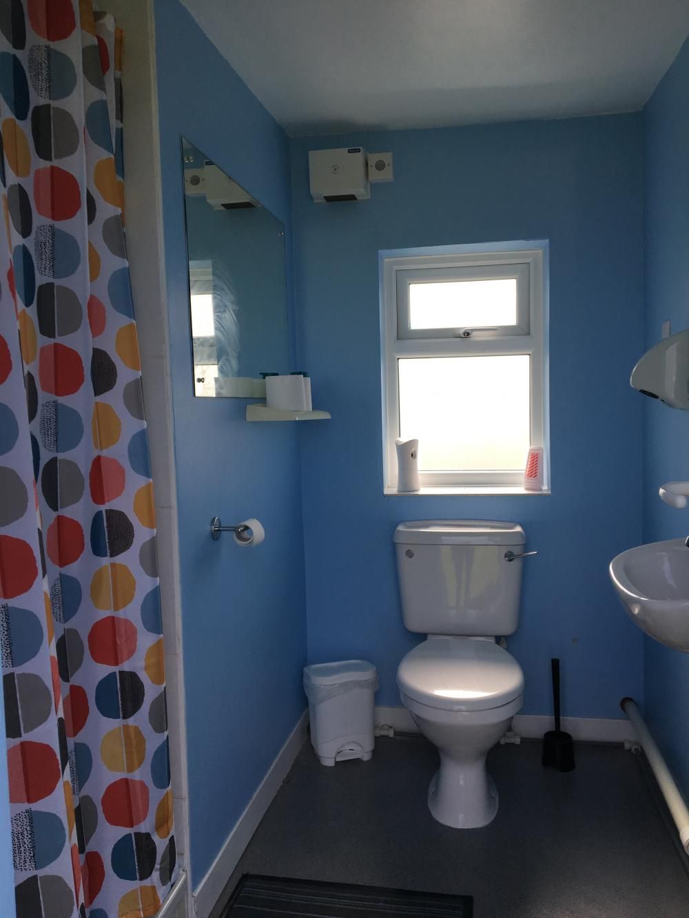 Blue bathroom with toilet, sink, window, and colorful shower curtain