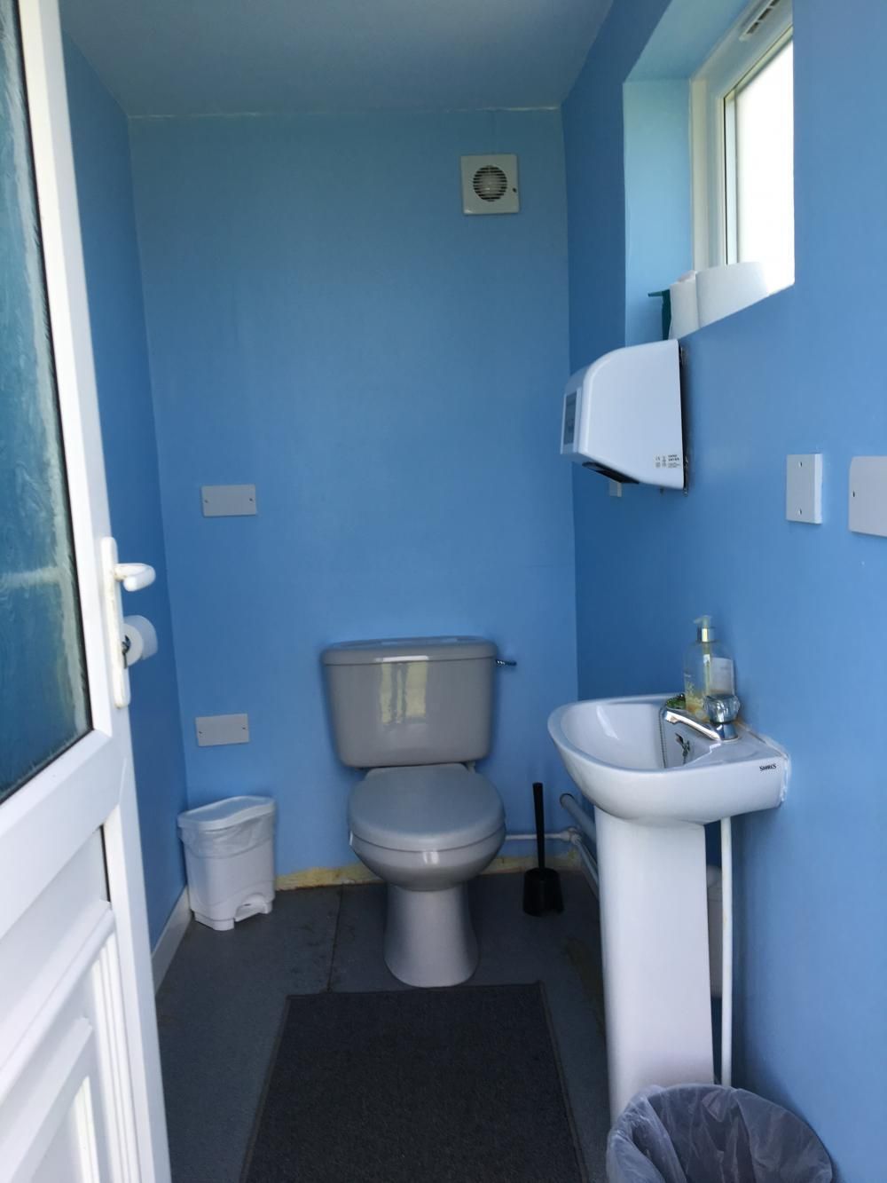 Small blue bathroom with a toilet, sink, wall mirror, and window.