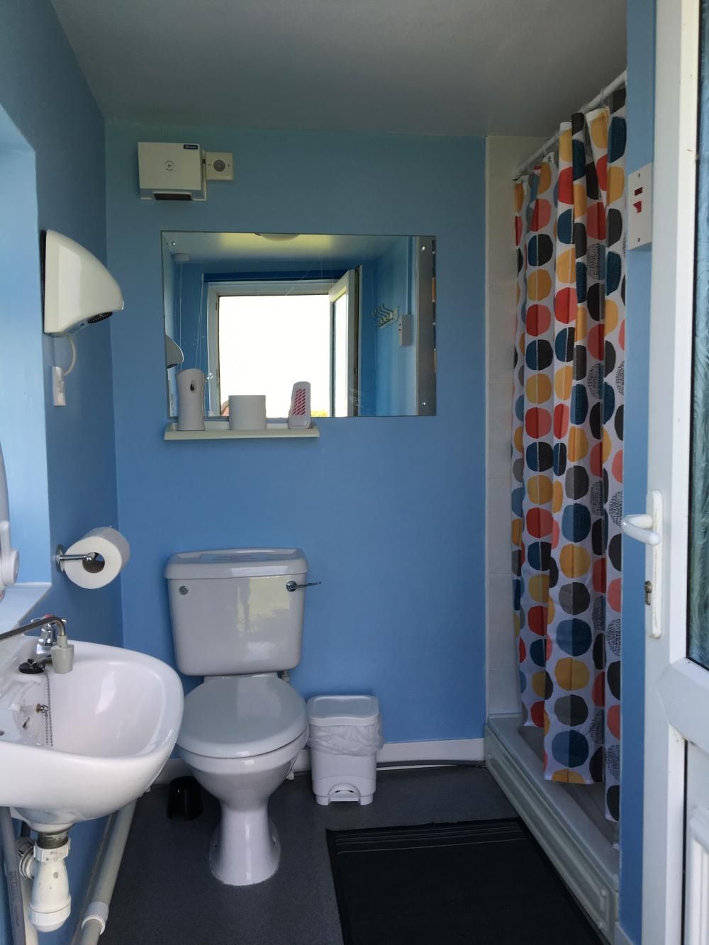 Small blue bathroom with toilet, sink, mirror, and colorful shower curtain