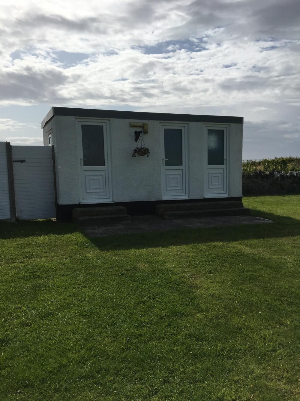 Small white mobile home on a grassy lawn under a cloudy sky