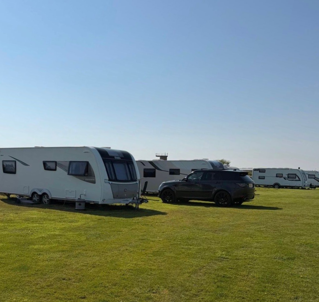 Camper trailers and a black SUV parked on a grassy field under a clear blue sky.