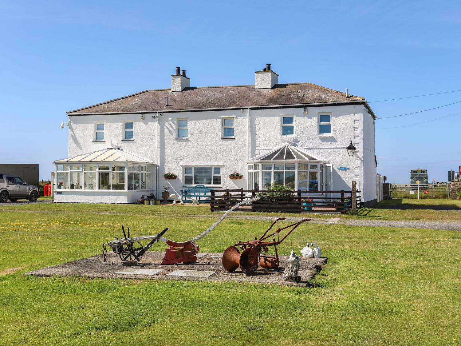 White seaside house with a green lawn and old farming tools displayed in front