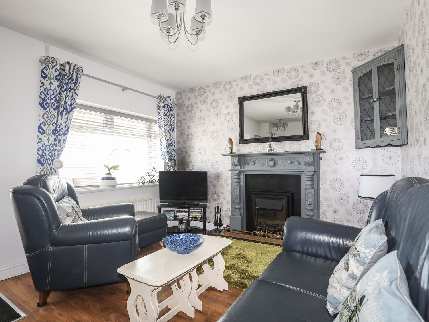 Cozy living room with black leather sofas, gray fireplace, blue accents, and a TV by the window
