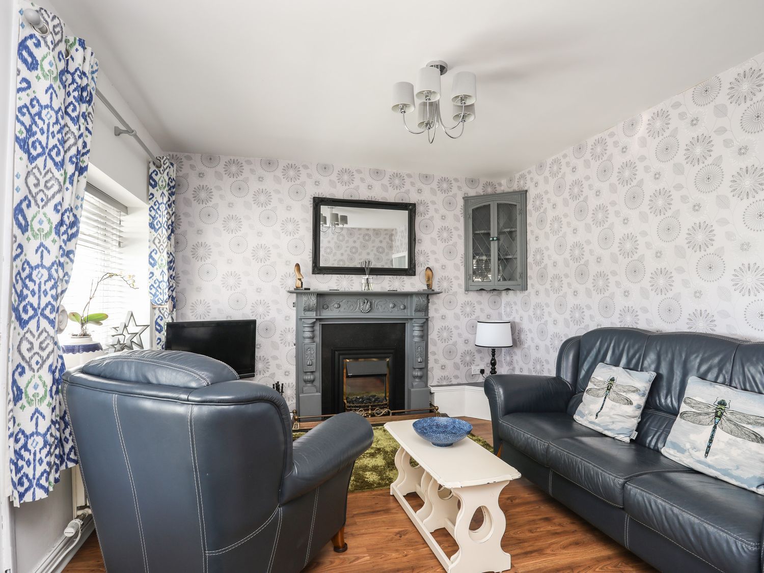 Bright living room with blue sofas, fireplace, patterned wallpaper, and white coffee table
