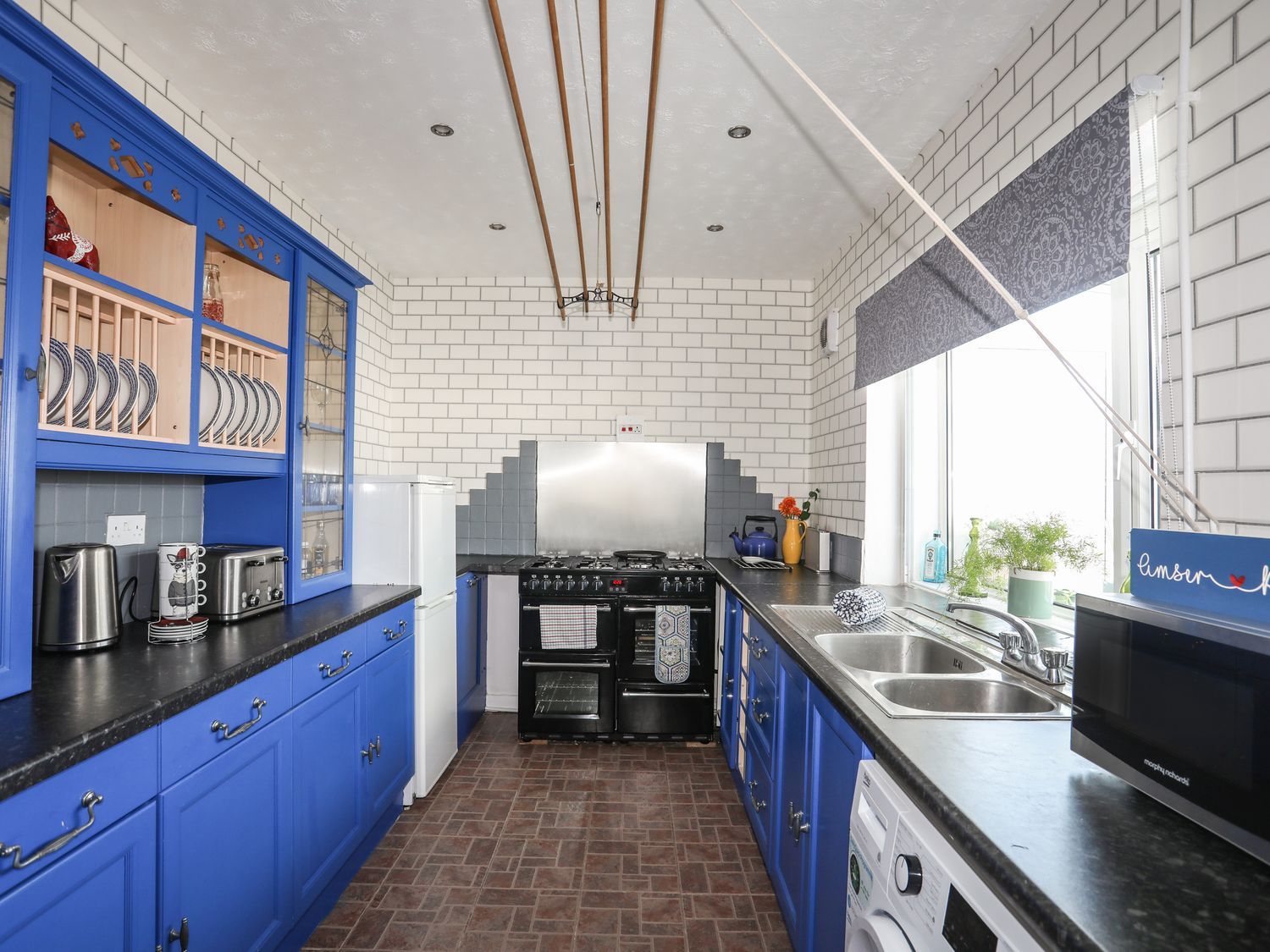Blue kitchen with black countertops, white brick walls, and a window over the sink.