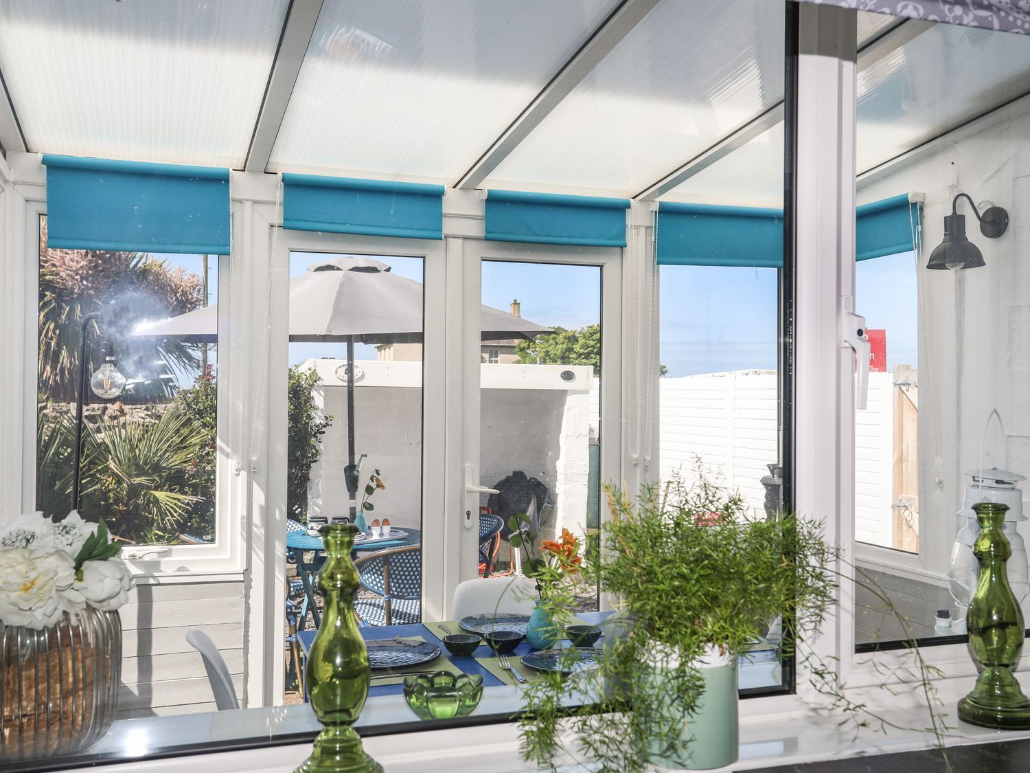 Bright sunroom with blue blinds, glass doors, and potted plants by a table.