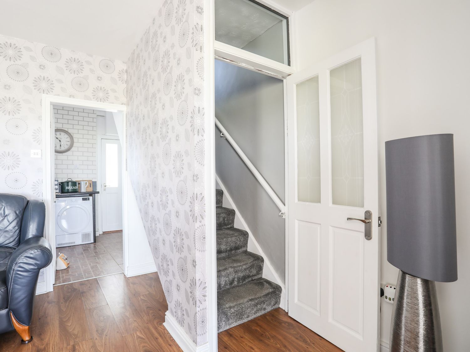 Living room with floral wallpaper, staircase, white door, and gray lamp beside a leather chair