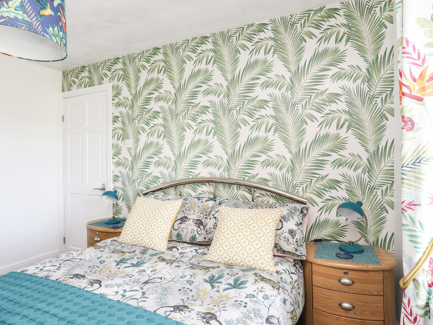 Bright bedroom with palm-leaf wallpaper, floral bedding, and wooden nightstands