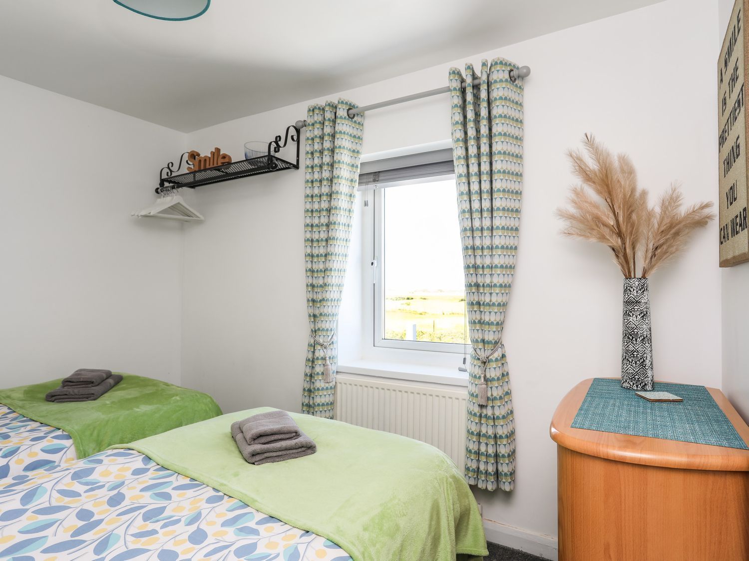 Bright bedroom with a bed, window, green accents, and a small dresser with dried flowers