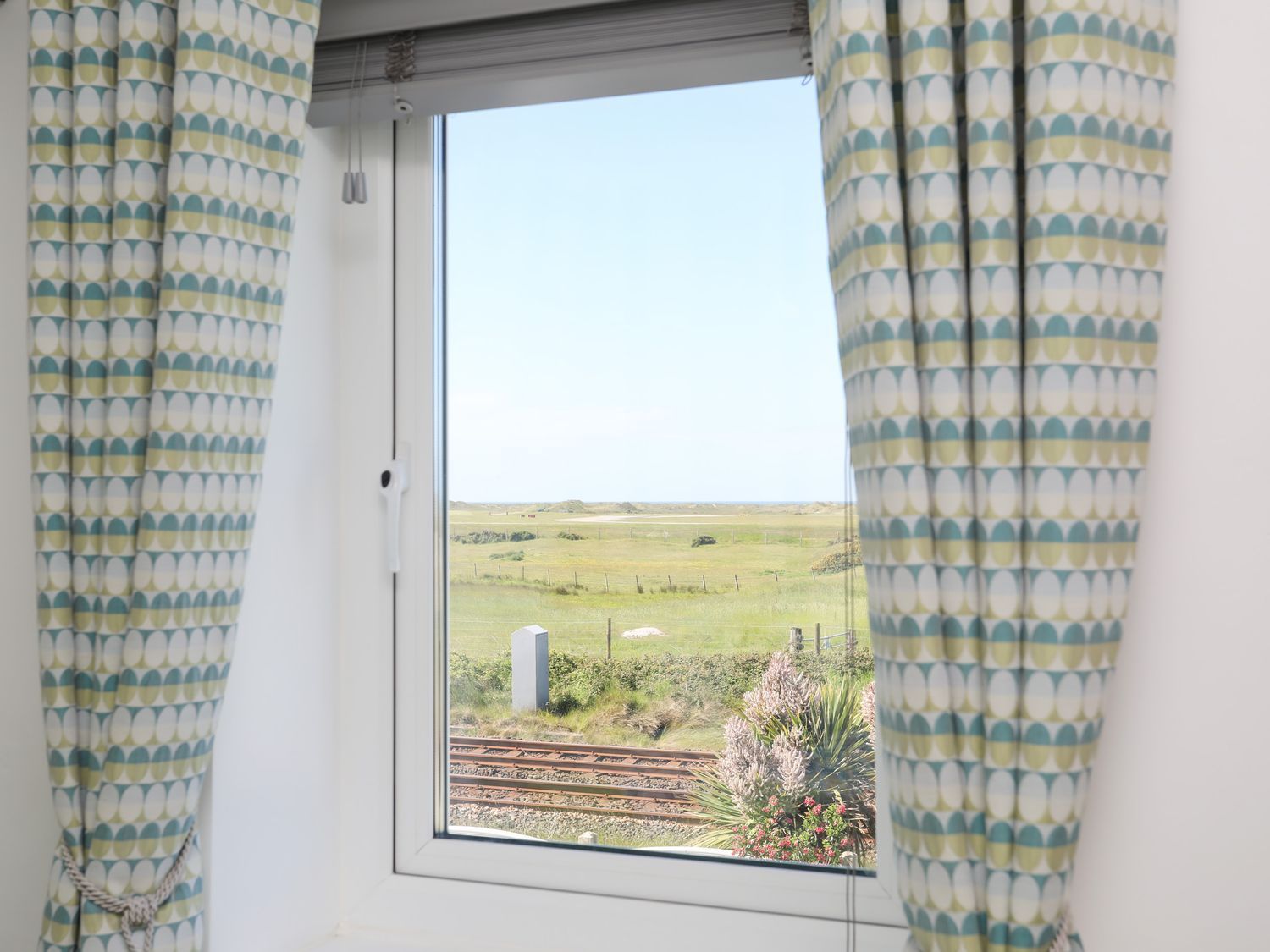 Open window with patterned curtains overlooking a grassy field and cloudy sky