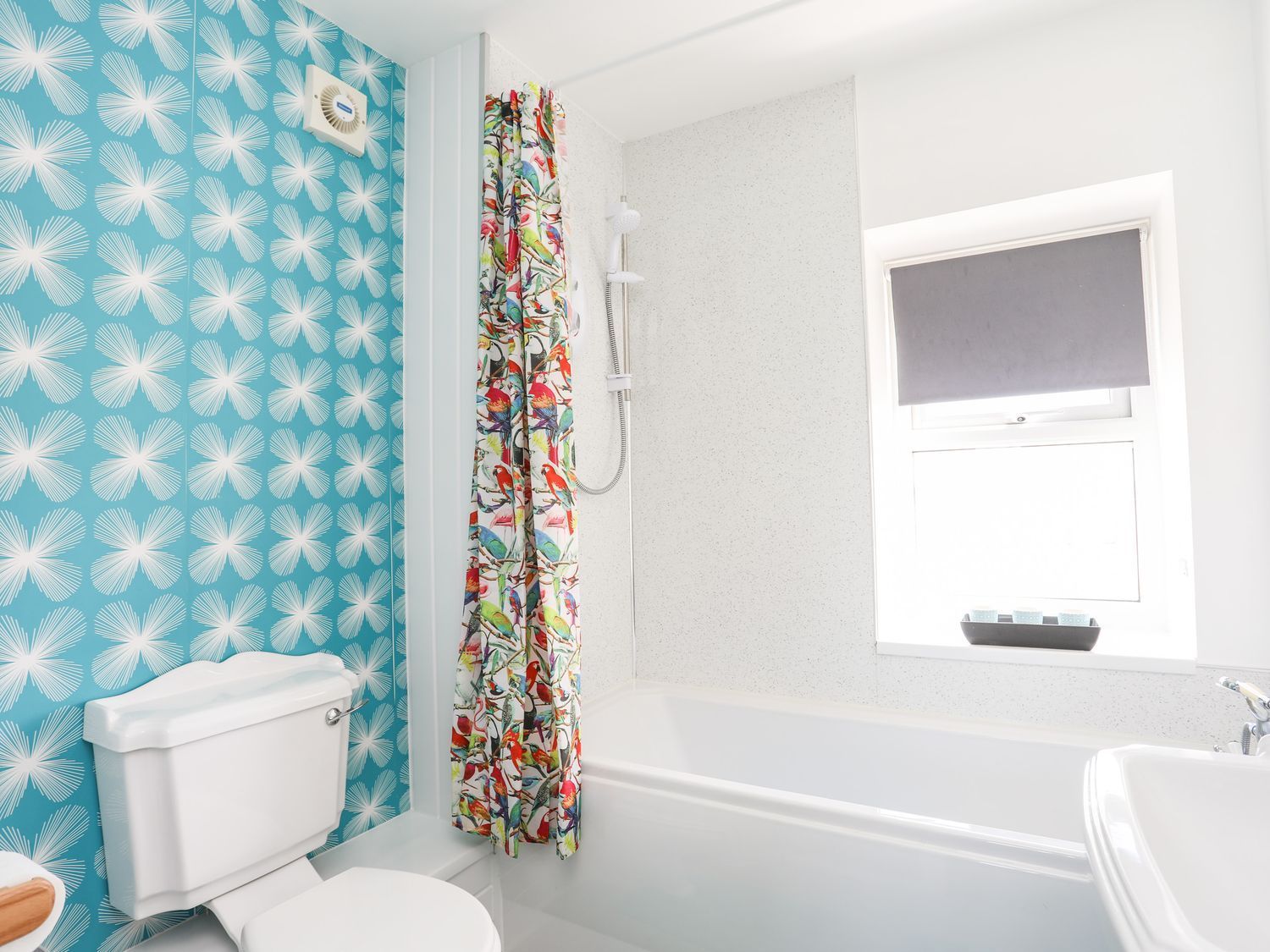 Bright bathroom with blue patterned wallpaper, floral shower curtain, white bathtub, and toilet.