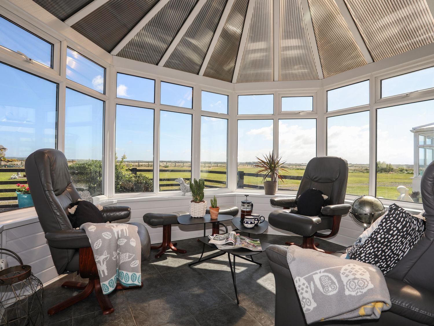 Sunroom with wicker chairs and a small table overlooking a grassy waterfront view