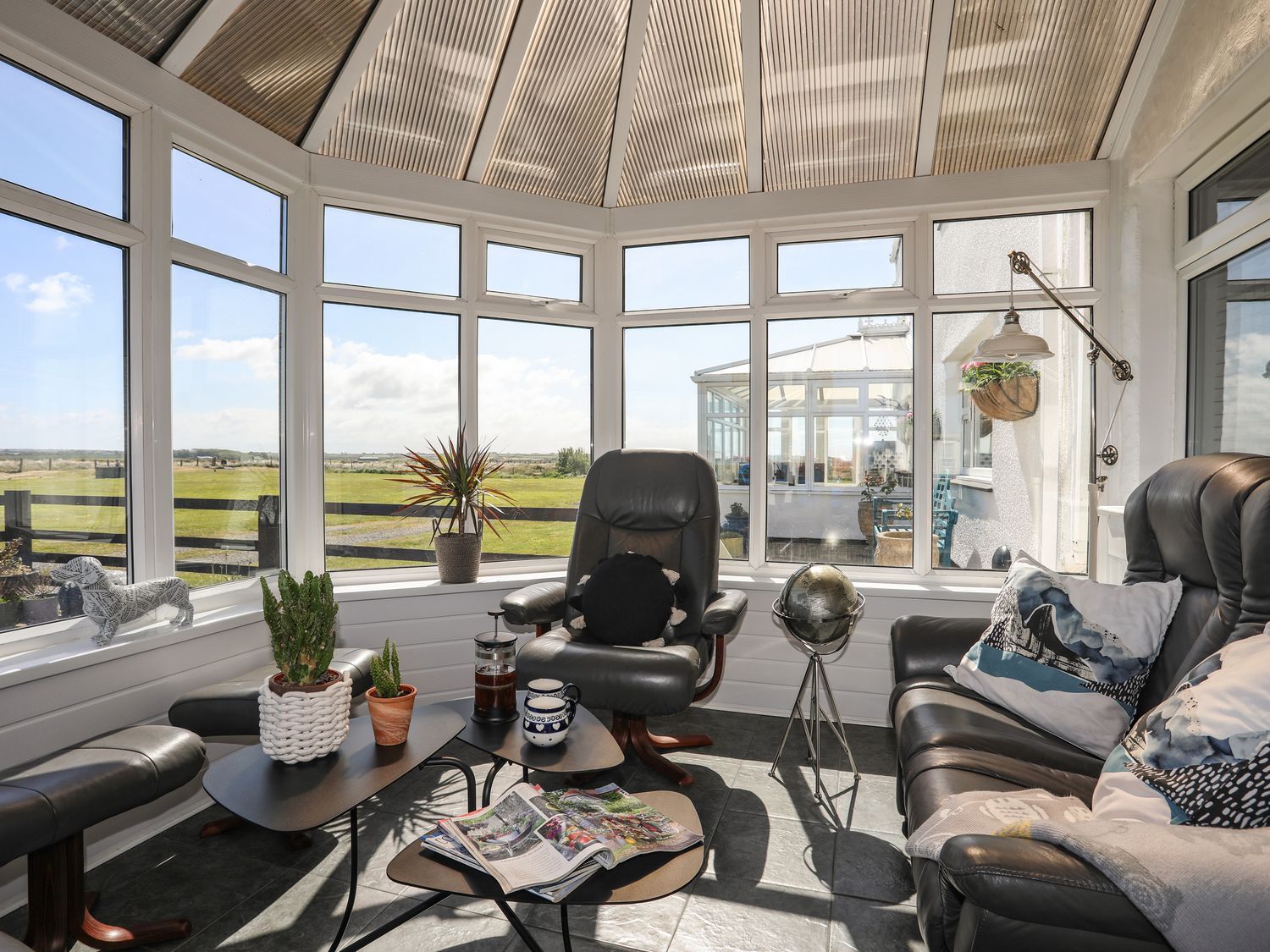 Bright sunroom with large windows, leather chairs, coffee table, and expansive countryside view
