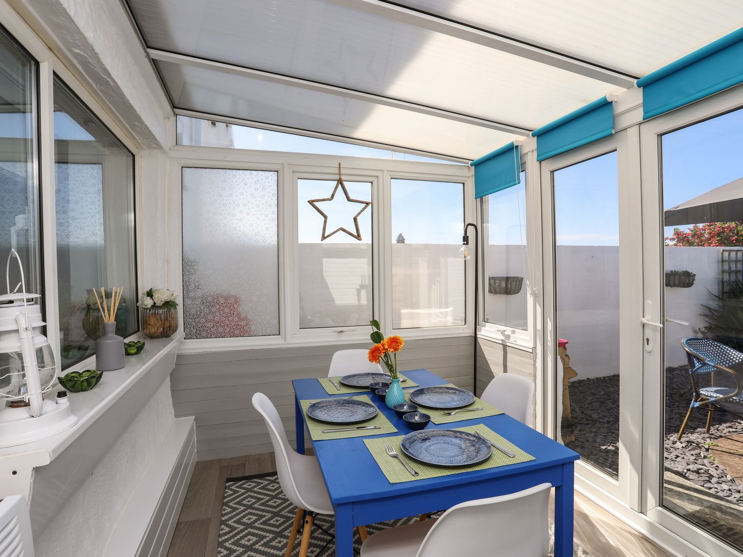 Bright sunroom with blue dining table, white chairs, and a star ornament on the window.