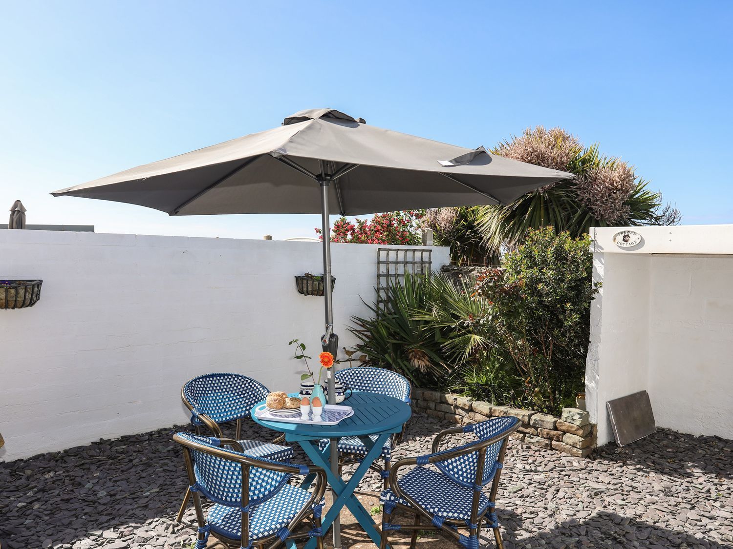 Blue patio table and chairs under a large umbrella in a sunny courtyard with white walls and plants