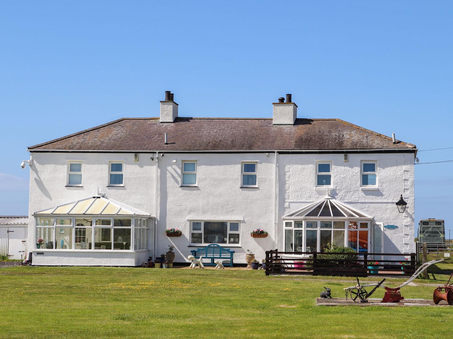 Large white seaside house with two chimneys, glass sunrooms, and a grassy front lawn under a blue sky