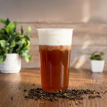 Iced coffee in a clear plastic cup with foam on a wooden table, coffee beans scattered around it