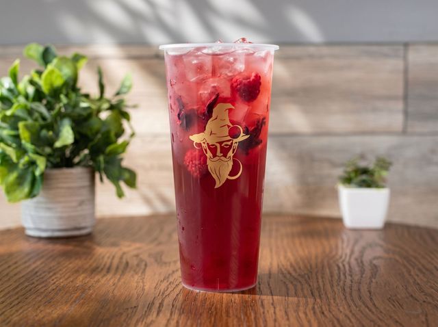 Tall red iced drink in a clear cup on a wooden table with blurred plants in the background