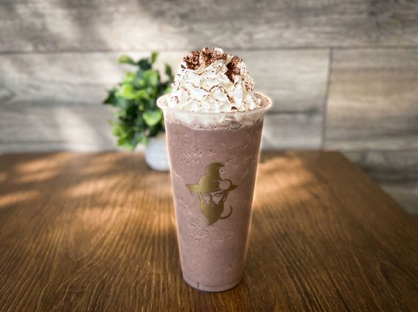 Chocolate smoothie topped with whipped cream in a clear cup on a wooden table