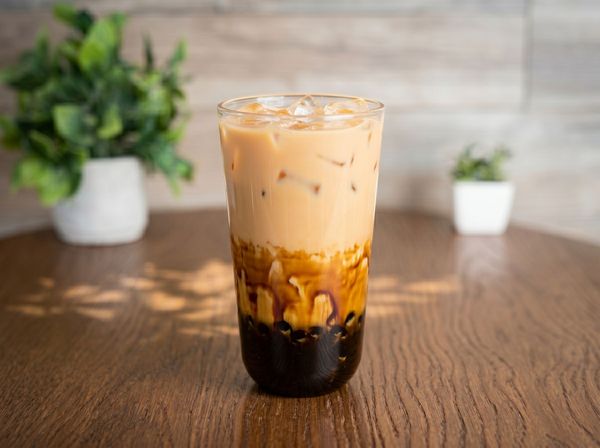 Iced layered coffee in a clear glass on a wooden table with blurred plants in the background