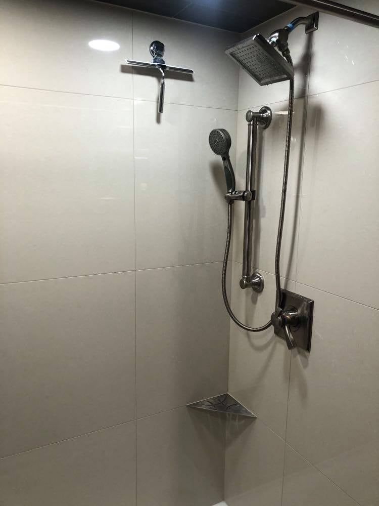 A shower with a shower head and a squeegee on the wall.