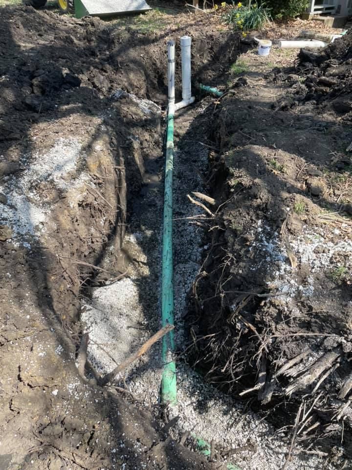 A green pipe is being installed in a hole in the ground.
