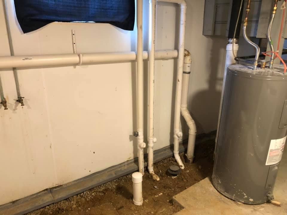 A water heater is sitting in a basement next to a window.