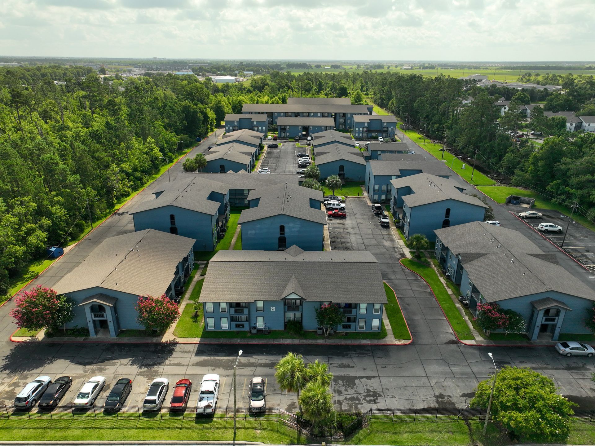 Aerial view of a low-rise apartment complex with parked cars, surrounded by trees.