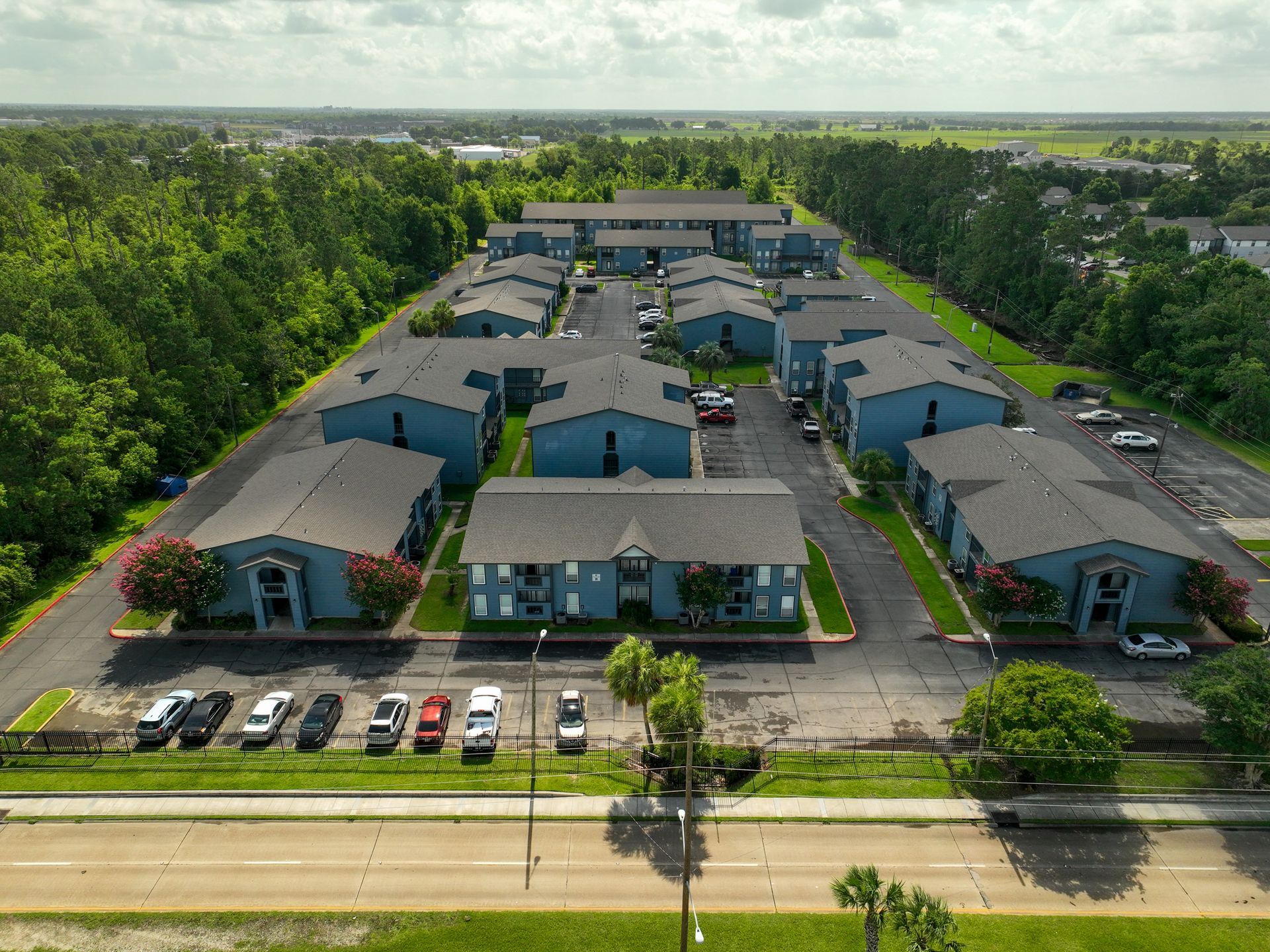 Aerial view of a large apartment complex with parking lots, surrounded by trees and open land
