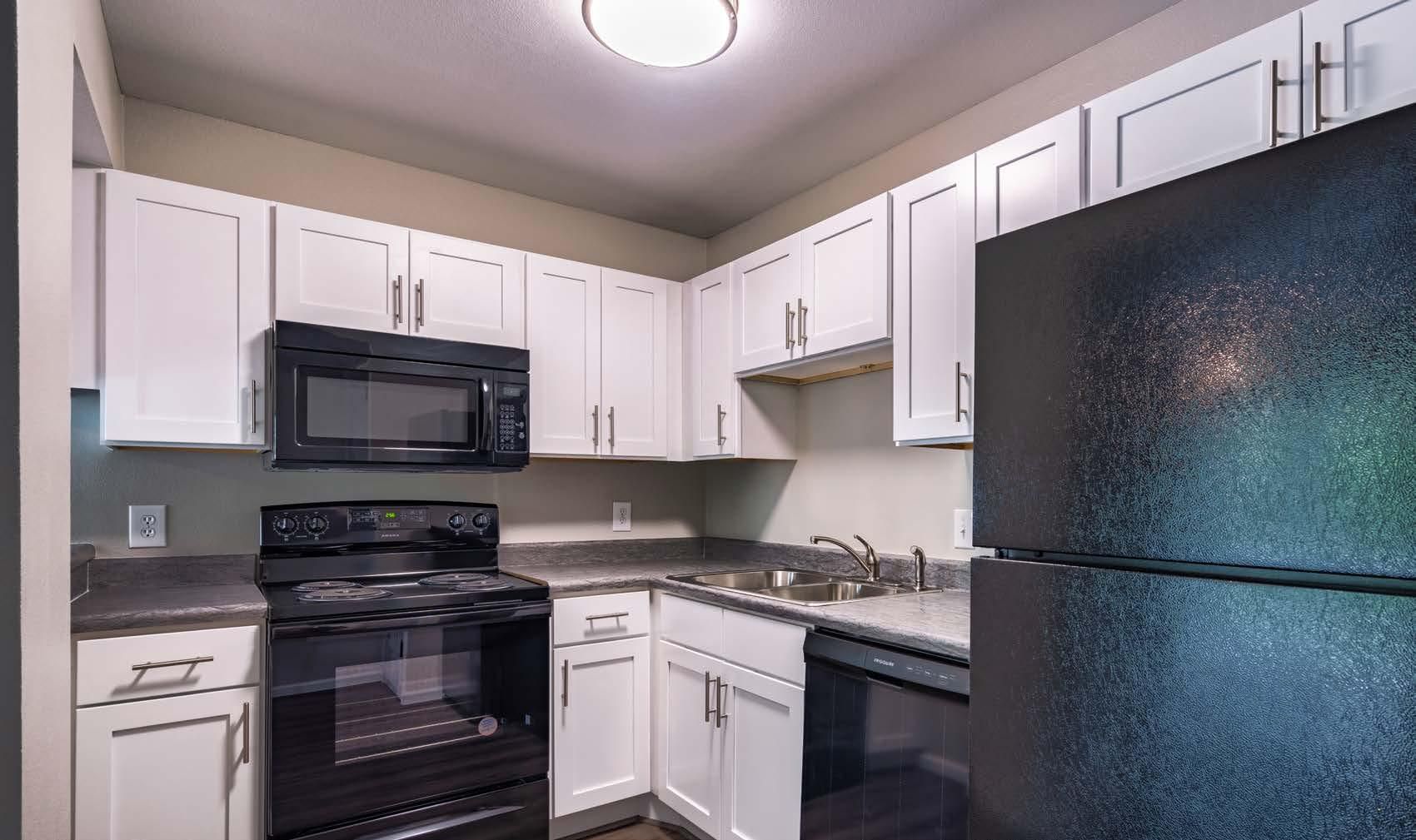 Small kitchen with white cabinets, black appliances, and a dark refrigerator
