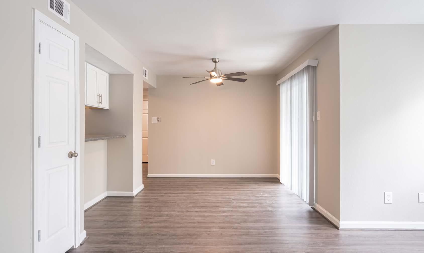 Empty beige living room with wood floors, ceiling fan, and sliding glass door