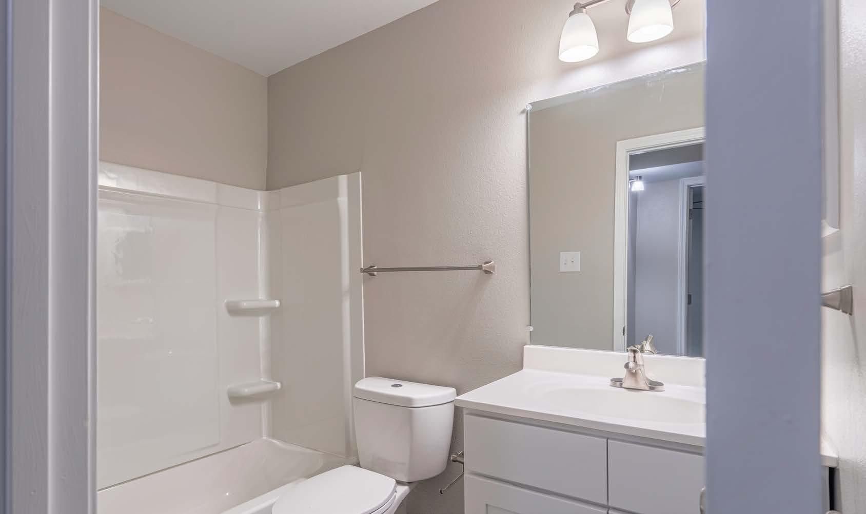 Bright white bathroom with bathtub, toilet, and vanity sink under mirror lights.