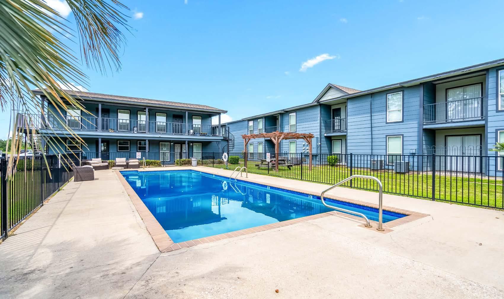 Apartment complex courtyard with a blue swimming pool and palm trees under a clear sky